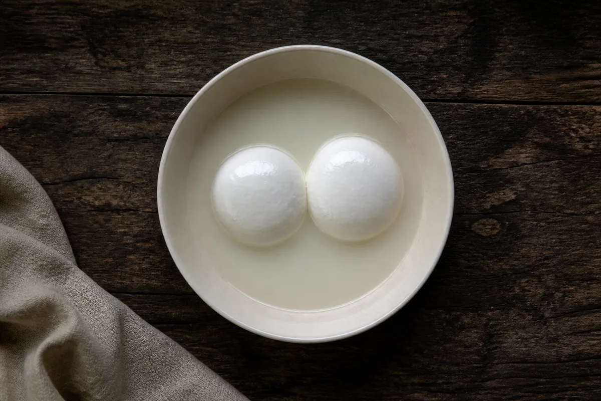 Deux boules blanches immergées dans un liquide clair, au fond d&rsquo;un bol de céramique unie, sur une table de bois brut