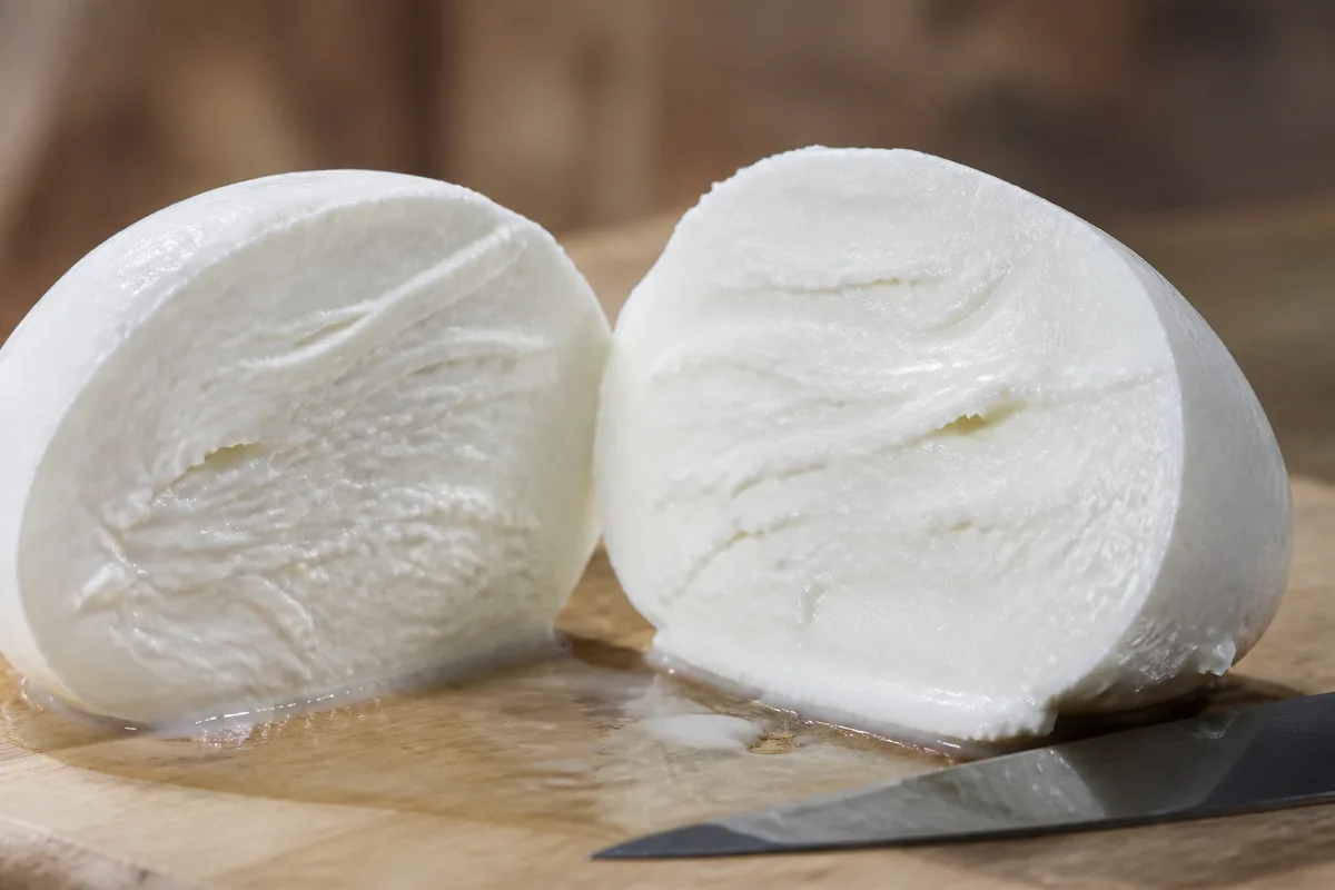 Boule blanche tranchée en deux sur une planche de bois clair, gouttes de lactosérum perlant sur la surface de coupe